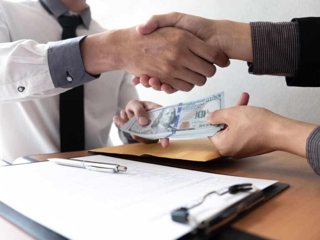 Two individuals shaking hands over a desk filled with cash