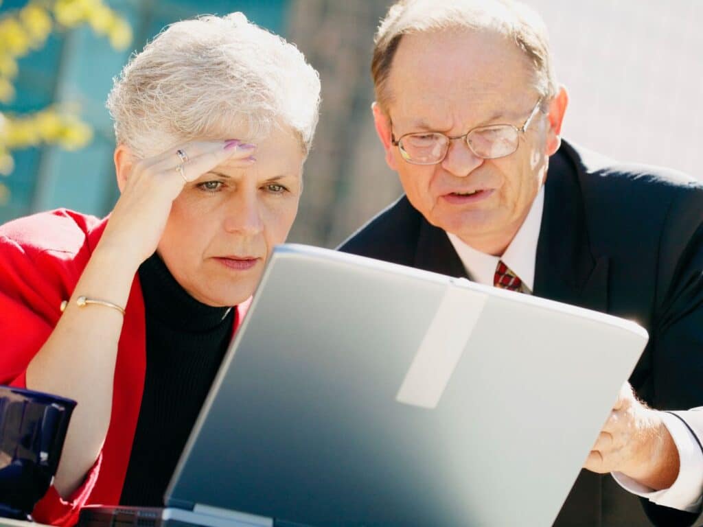 A man and woman are seated together, intently focused on a laptop screen in a collaborative setting